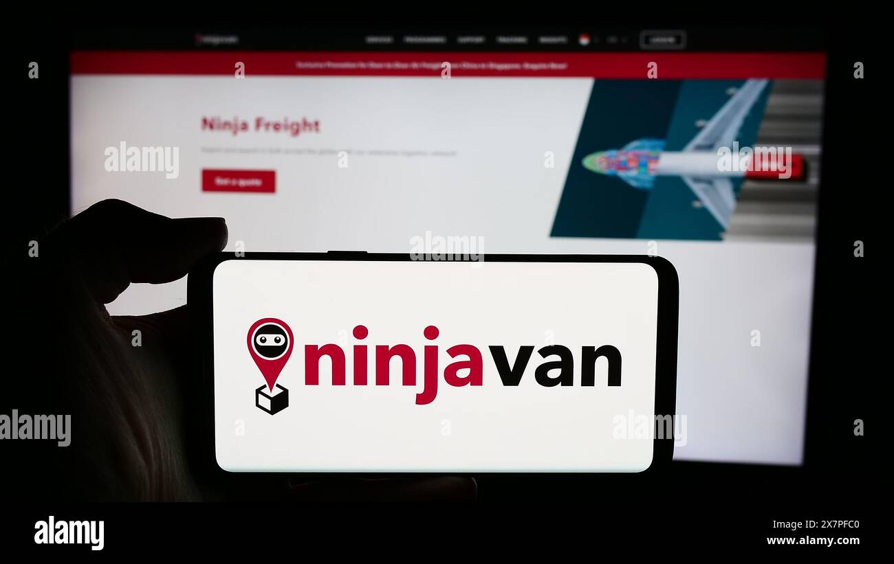 Personne tenant le téléphone portable avec le logo de la société de livraison singapourienne Ninja Logistics Pte. Ltd en face de la page Web. Concentrez-vous sur l'affichage du téléphone. Banque D'Images