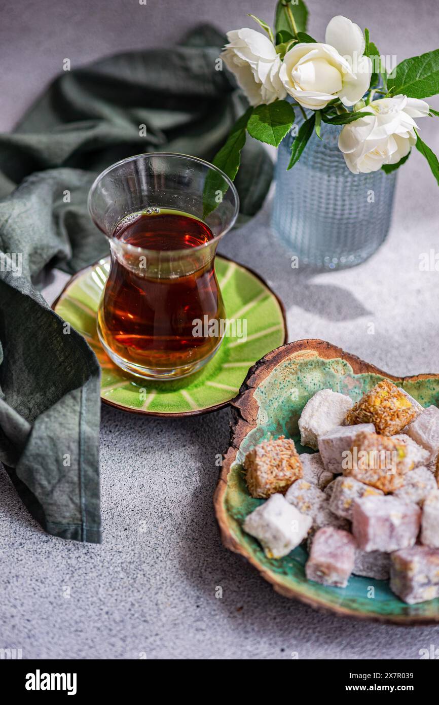 Assortiment de délices traditionnels turcs sur une assiette en céramique à côté d'un verre de thé noir, avec un vase de roses blanches en arrière-plan Banque D'Images