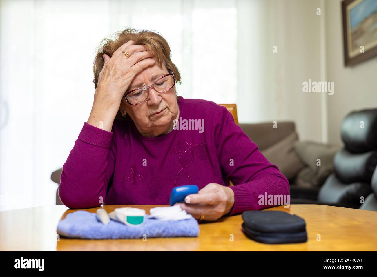 Une femme âgée dans un pull violet semble inquiète alors qu'elle vérifie son taux de glucose dans le sang, indiquant des symptômes d'hypoglycémie Banque D'Images