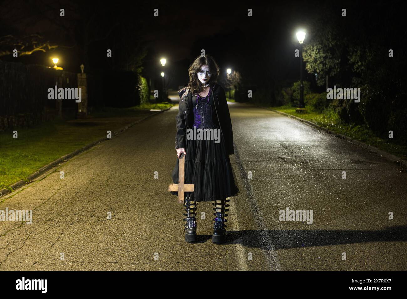 Une jeune femme vêtue d'une tenue gothique, avec un maquillage d'Halloween, se tient dans une rue déserte la nuit, regardant la caméra d'une manière obsédante. Banque D'Images