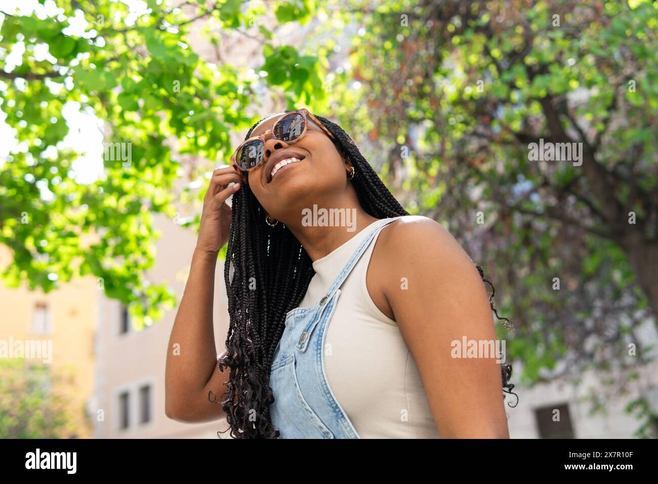 Jeune femme souriante avec des tresses et des lunettes de soleil expérimentant les vibrations joyeuses d'un été à Barcelone Banque D'Images
