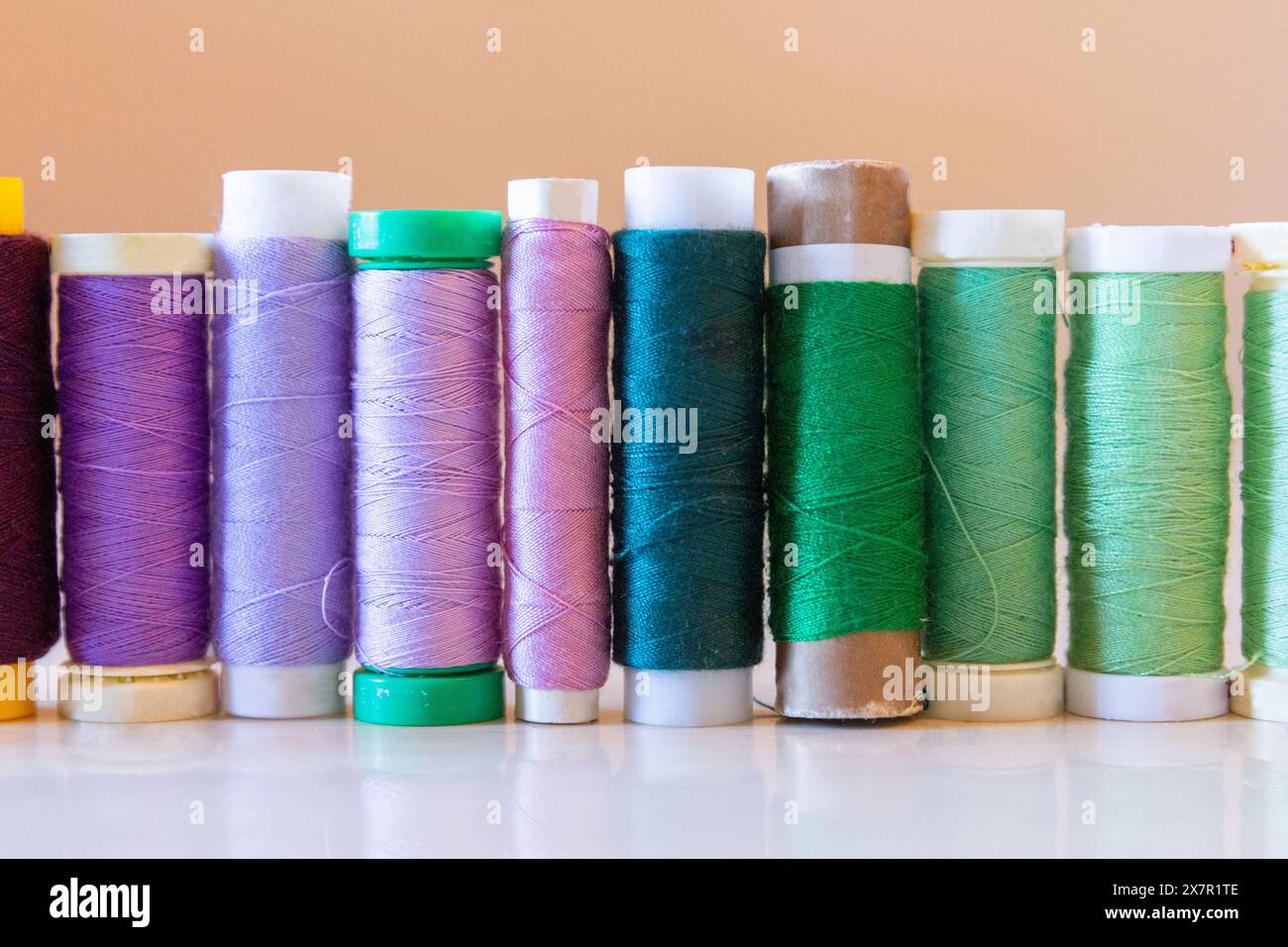 Une rangée soignée de bobines de fil dans différentes nuances de violet et de vert se dresse sur un fond pâle, mettant en évidence les essentiels de la couture Banque D'Images