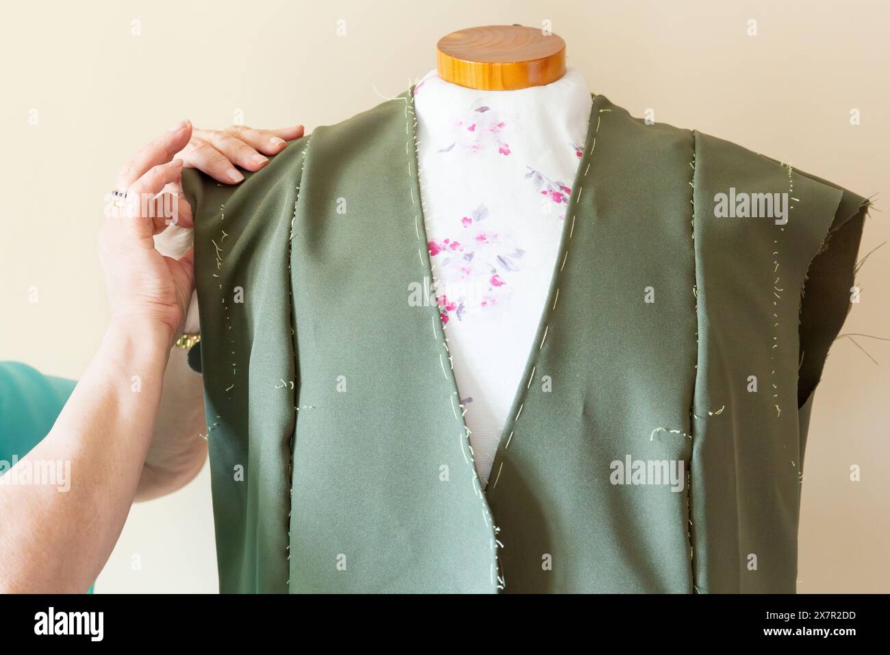 Gros plan d'un tailleur portant un vêtement vert sur un mannequin, avec doublure florale et points de couture à la main visibles Banque D'Images