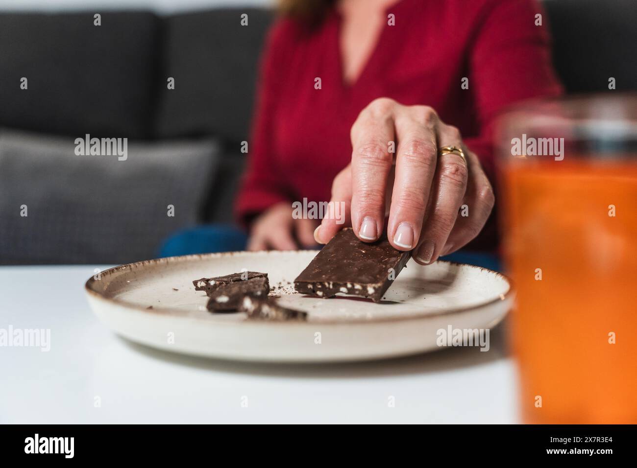 Gros plan de la main d'une femme sélectionnant un morceau de chocolat dans une assiette, un remède rapide pour l'hypoglycémie, montrant une gestion diététique pratique à la veille Banque D'Images