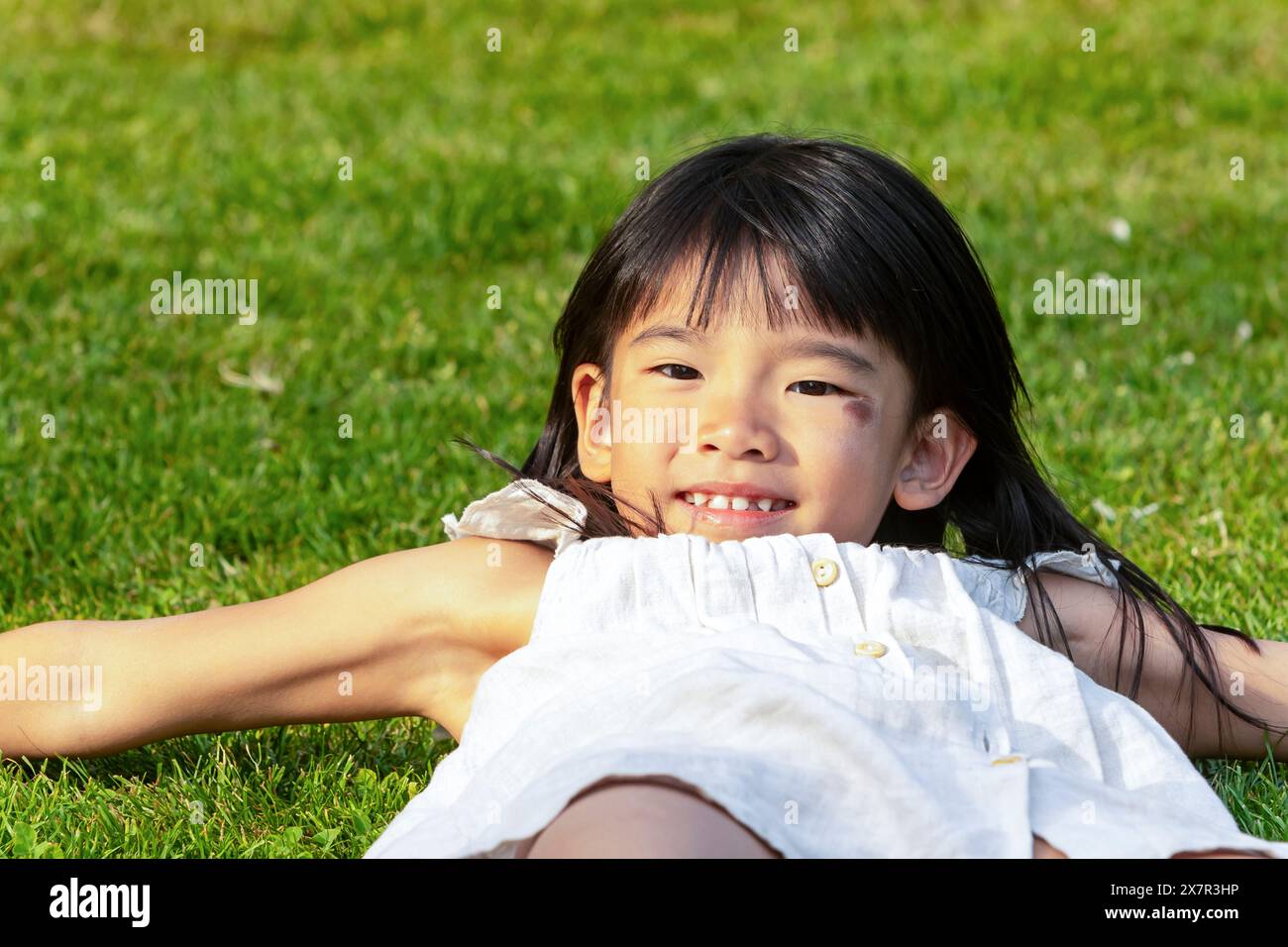 Une jeune fille asiatique est allongée sur l’herbe, souriante, lors de vacances en famille en Europe, incarnant la joie du voyage et de l’exploration culturelle Banque D'Images