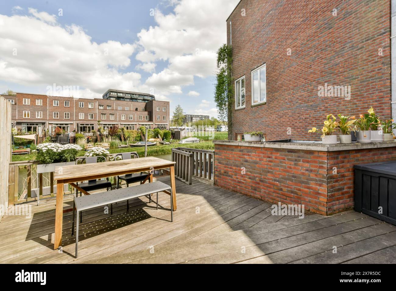 Un patio extérieur urbain confortable avec une table à manger en bois et des chaises, sur fond de bâtiments résidentiels en briques et une garde commune luxuriante Banque D'Images