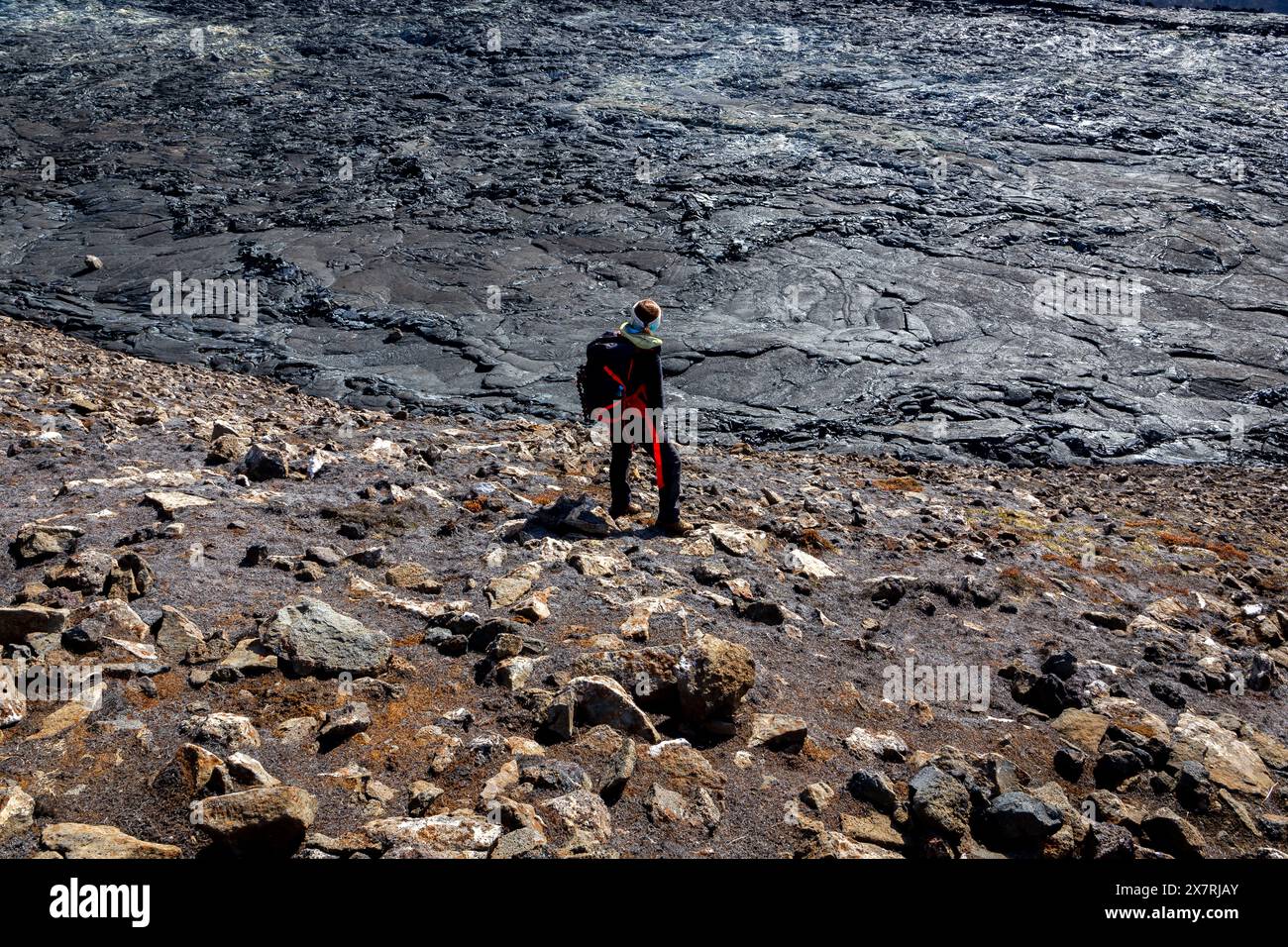 Touriste femme avec sac à dos debout sur les roches de basalte en fusion dans le champ de lave du volcan Fagradalsfjall, observant le paysage volcanique, Islande. Banque D'Images