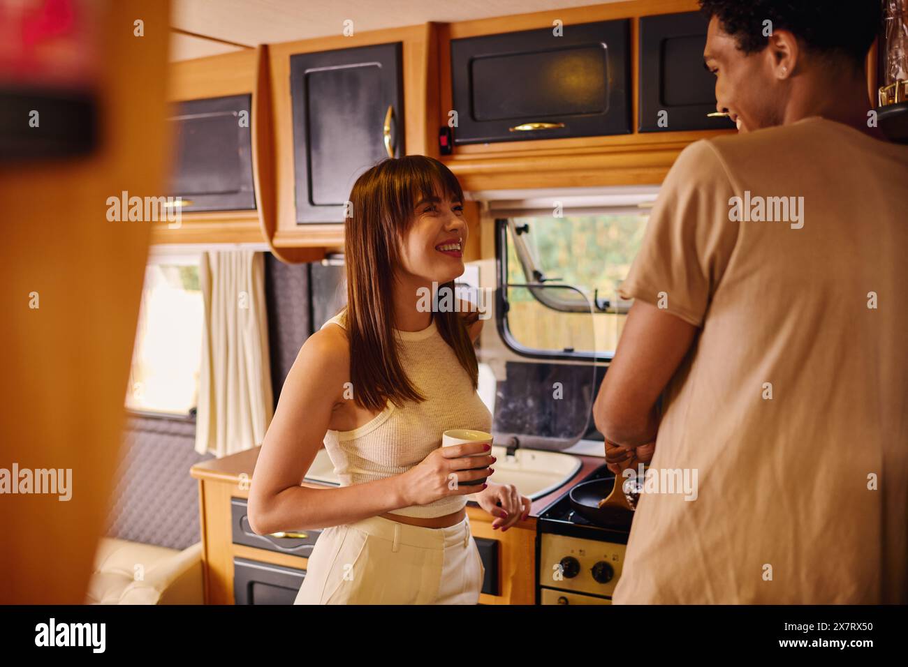 Une femme élégante dans une robe blanche debout à côté d'un homme dans une cuisine, partageant un moment dans leur environnement élégant. Banque D'Images