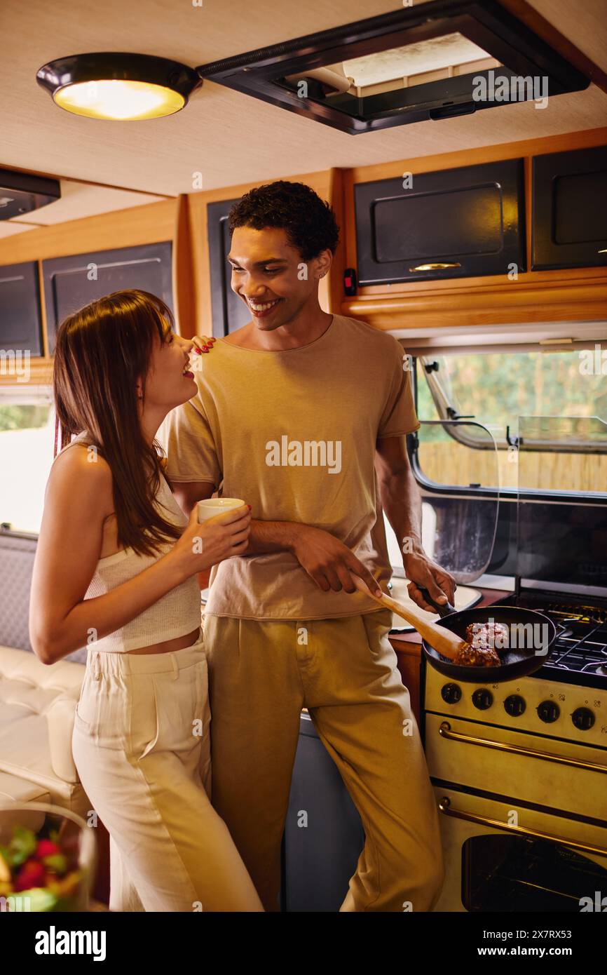 Un couple interracial se tient côte à côte devant un poêle, engagé dans une expérience culinaire partagée. Banque D'Images