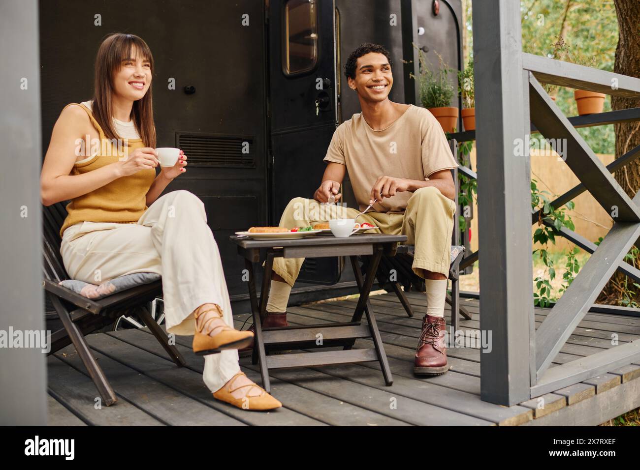 Un couple interracial se détend ensemble sur un porche confortable, appréciant les uns les autres compagnie dans un cadre paisible. Banque D'Images
