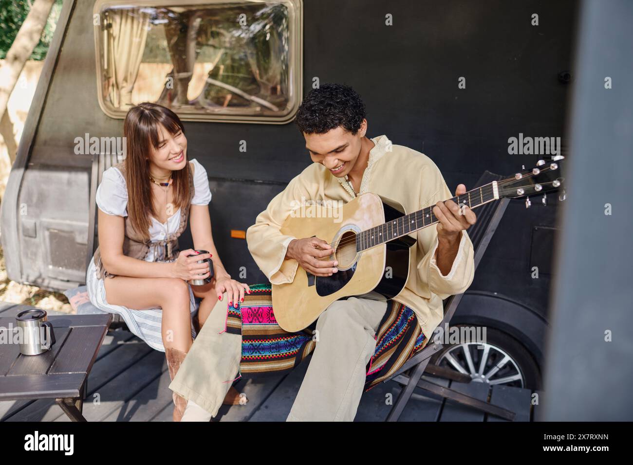 Un homme jouant de la guitare à côté d'une femme dans un cadre romantique entouré par la nature, appréciant les uns les autres compagnie. Banque D'Images