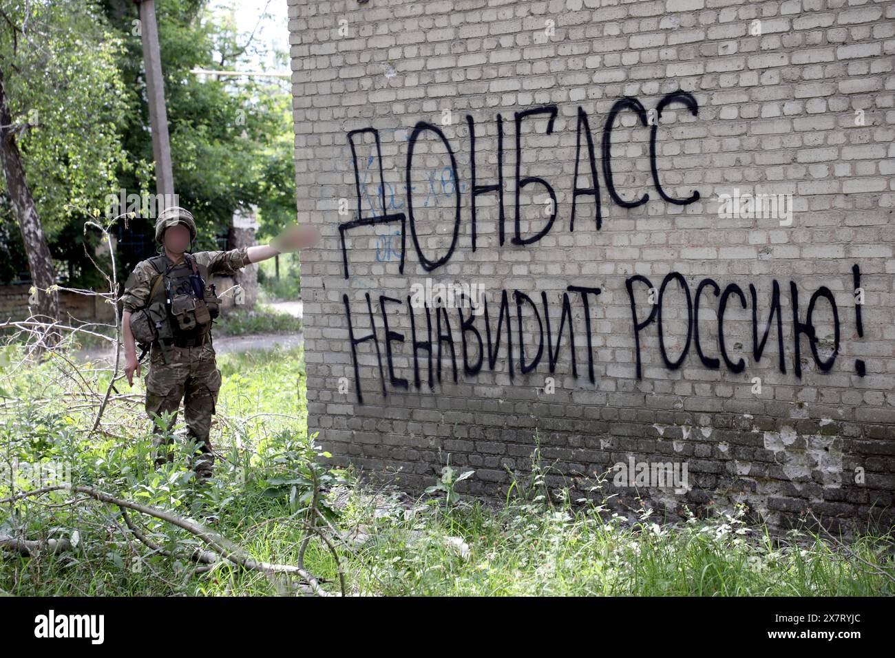 ChasIV YAR, UKRAINE - 18 MAI 2024 - Un soldat pointe la phrase en russe “le Donbass déteste la Russie!” Sur le mur d'un bâtiment, Chasiv Yar, région de Donetsk, Ukraine orientale. Banque D'Images