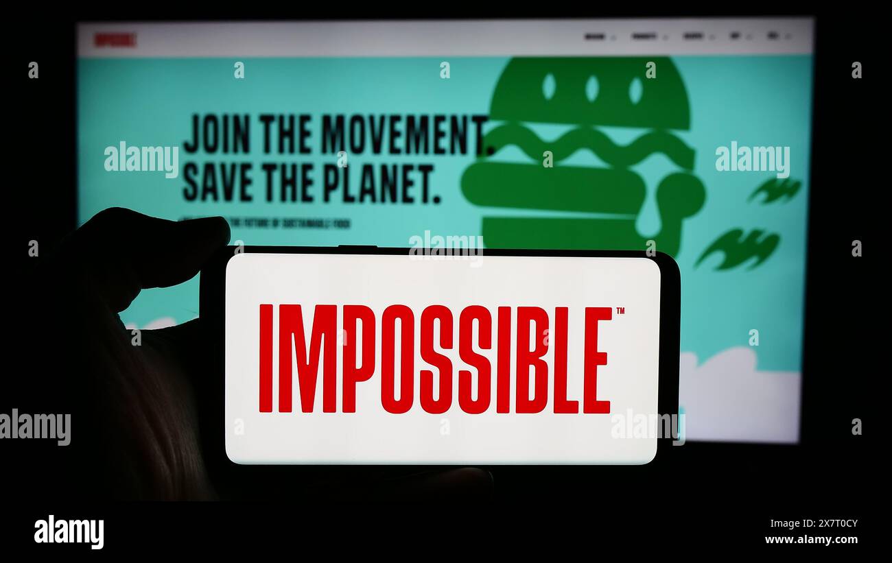 Personne tenant le téléphone portable avec le logo de la société américaine de remplacement de viande impossible Foods Inc devant la page Web de l'entreprise. Concentrez-vous sur l'affichage du téléphone. Banque D'Images