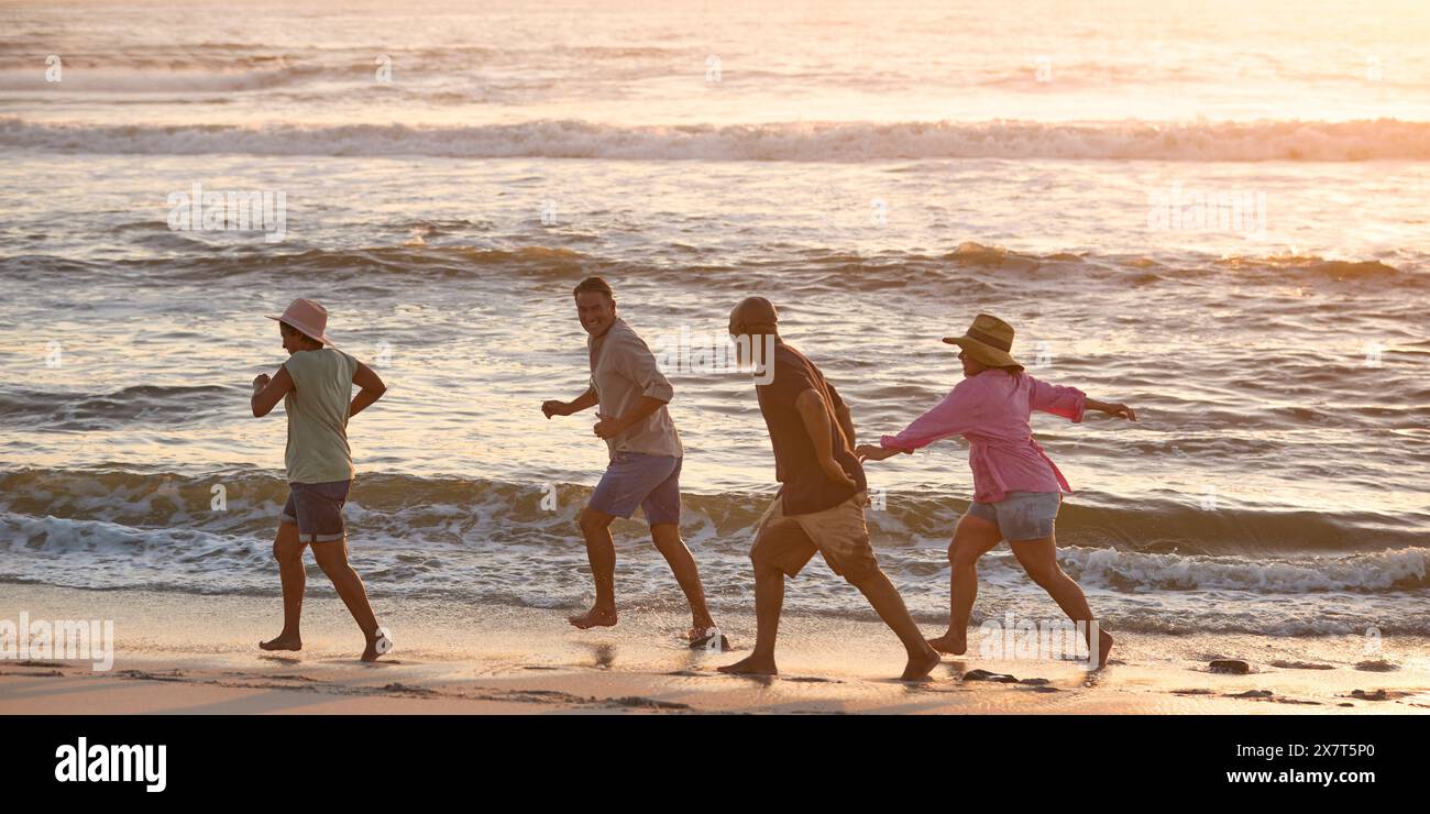 Couple d'âge mûr avec des amis en vacances marchant à travers les vagues sur Beach Shoreline au coucher du soleil Banque D'Images