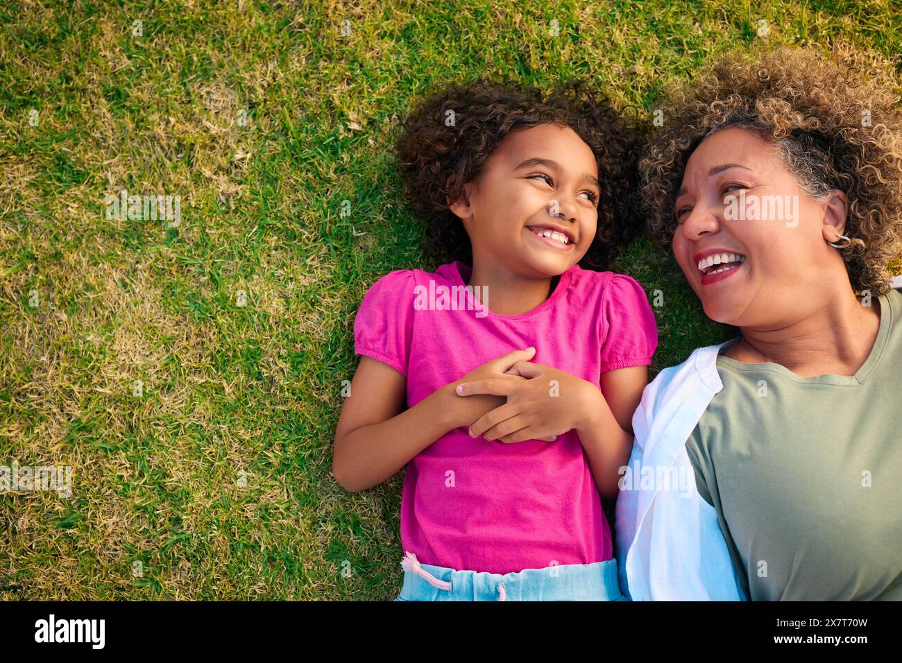 Regardant grand-mère avec petite-fille allongée à l'extérieur sur herbe regardant la caméra Banque D'Images