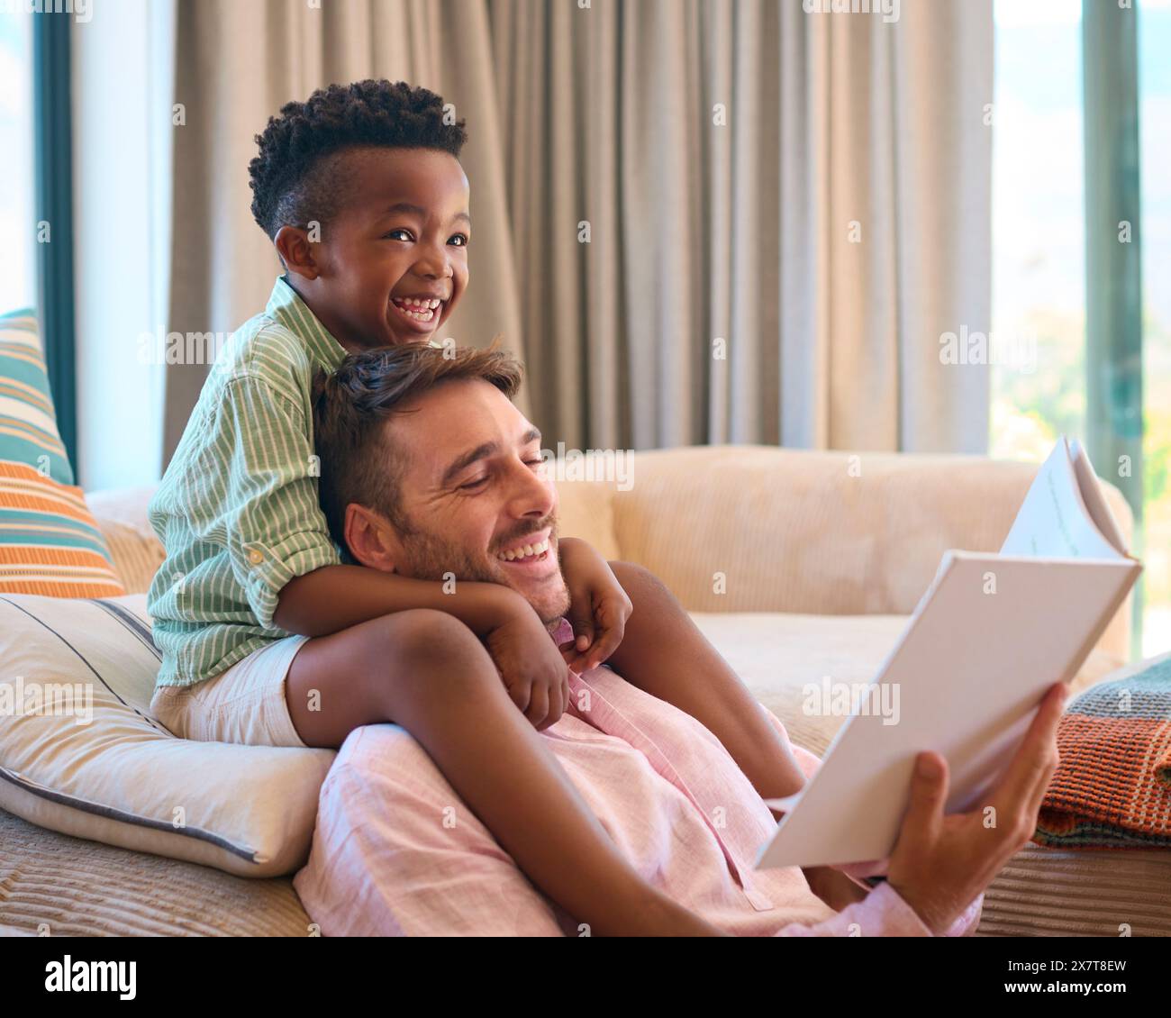 Famille multiraciale à la maison avec père et fils lisant le livre ensemble Banque D'Images