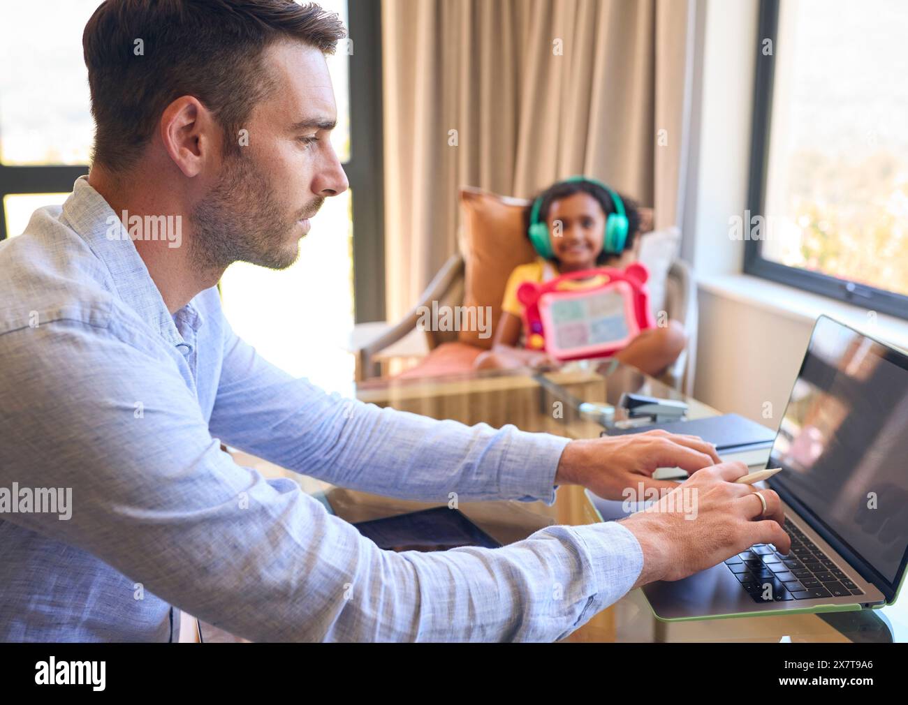 Père travaillant à domicile sur tablette numérique comme fille écoute de la musique et joue en arrière-plan Banque D'Images