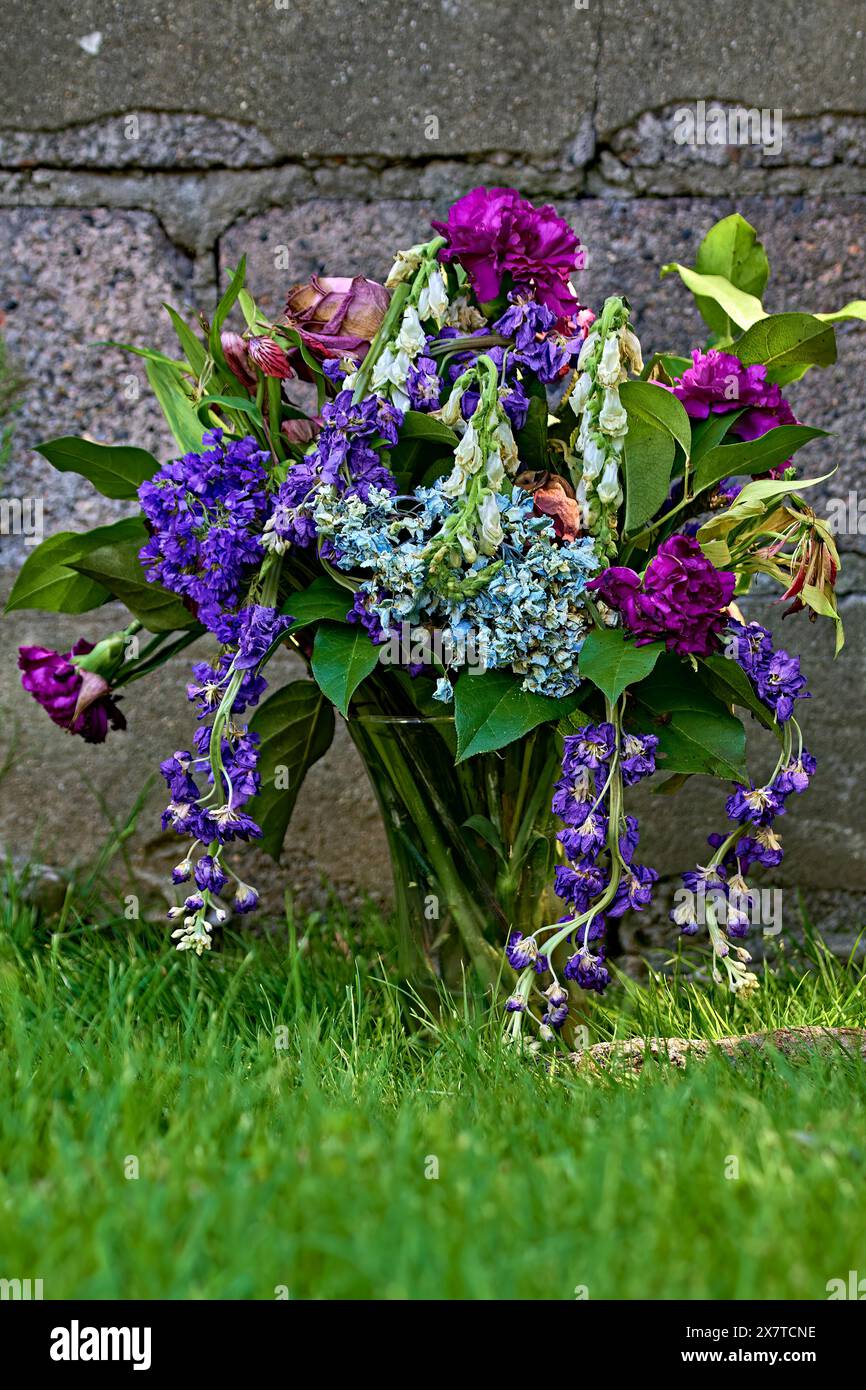 Une photo couleur d'un bouquet de fleurs mortes devant un mur de blocs de cendre. Banque D'Images