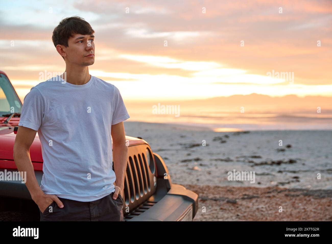 Jeune homme debout en voiture garée à la plage regardant le lever du soleil Banque D'Images Jeune homme debout en voiture garée à la plage regardant le lever du soleil Banque D'Images