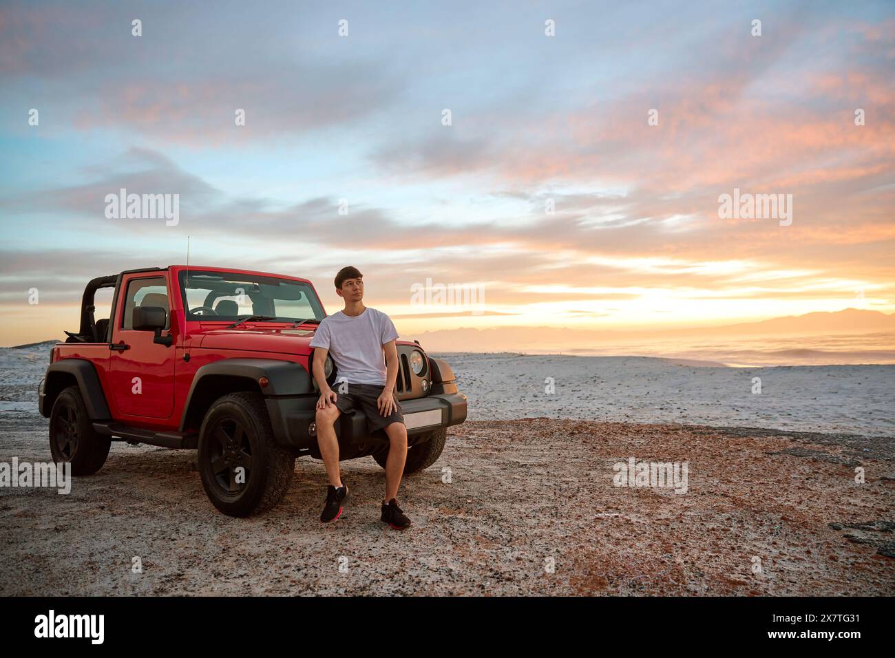 Jeune homme debout en voiture garée à la plage regardant le lever du soleil Banque D'Images Jeune homme debout en voiture garée à la plage regardant le lever du soleil Banque D'Images