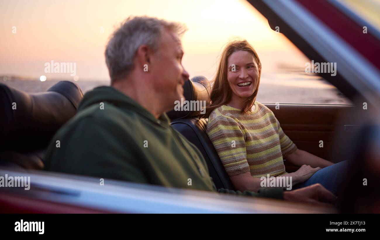 Couple senior retraité en vacances assis dans une voiture de sport classique à Beach Watching Sunrise Banque D'Images