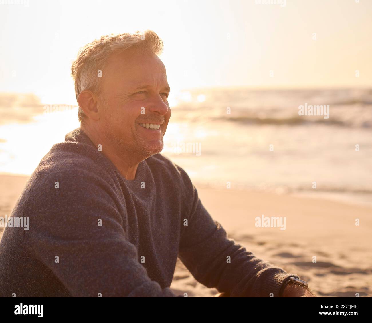 Homme senior à la retraite en vacances assis sur la plage Shoreline regardant le lever du soleil Banque D'Images