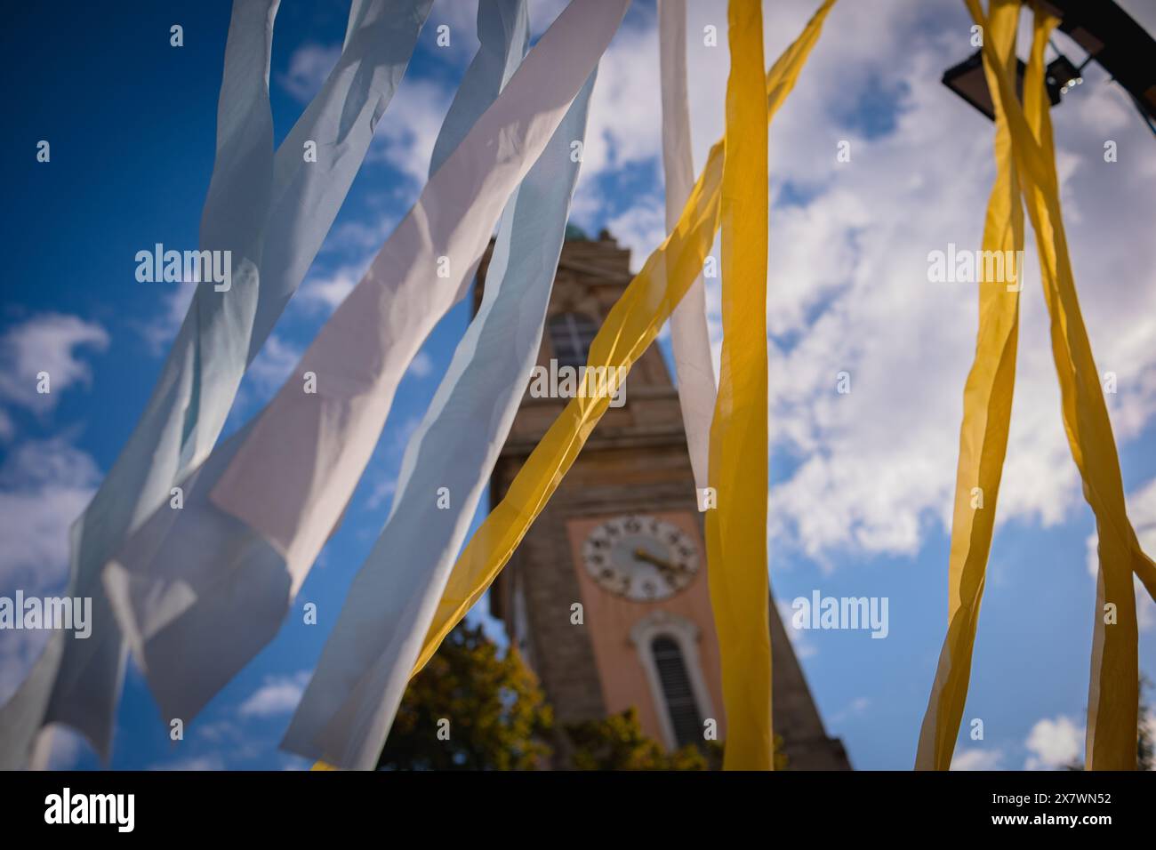 Des rubans de tissu jaunes et bleus flottent dans le vent sur le fond d'un ciel bleu et d'une ancienne tour de l'horloge. Banque D'Images