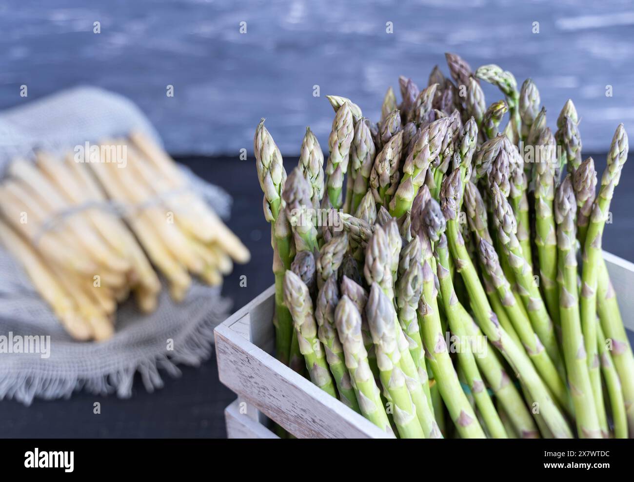 Gros plan d'asperges vertes dans une caisse grise avec des asperges blanches en arrière-plan, nettoyées après la récolte Banque D'Images