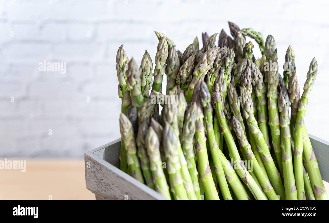 Contre un mur de briques blanches quelques tiges d'asperges vertes fraîches dans une caisse en bois grise prête à être cuite Banque D'Images