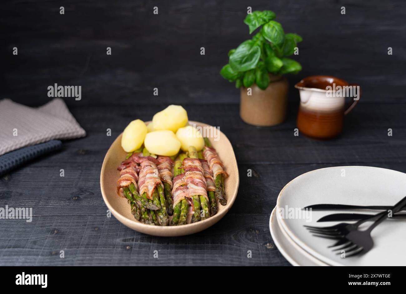 Asperges vertes cuites cuites enveloppées dans du bacon et servies avec des pommes de terre bouillies sur de belles assiettes beiges sur fond sombre Banque D'Images