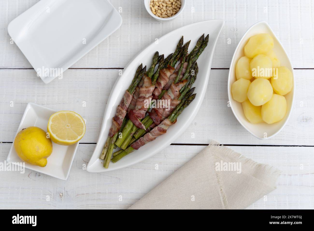 Asperges vertes cuites au four enveloppées dans du bacon et servies avec des pommes de terre bouillies sur de belles assiettes blanches sur une surface en bois clair Banque D'Images