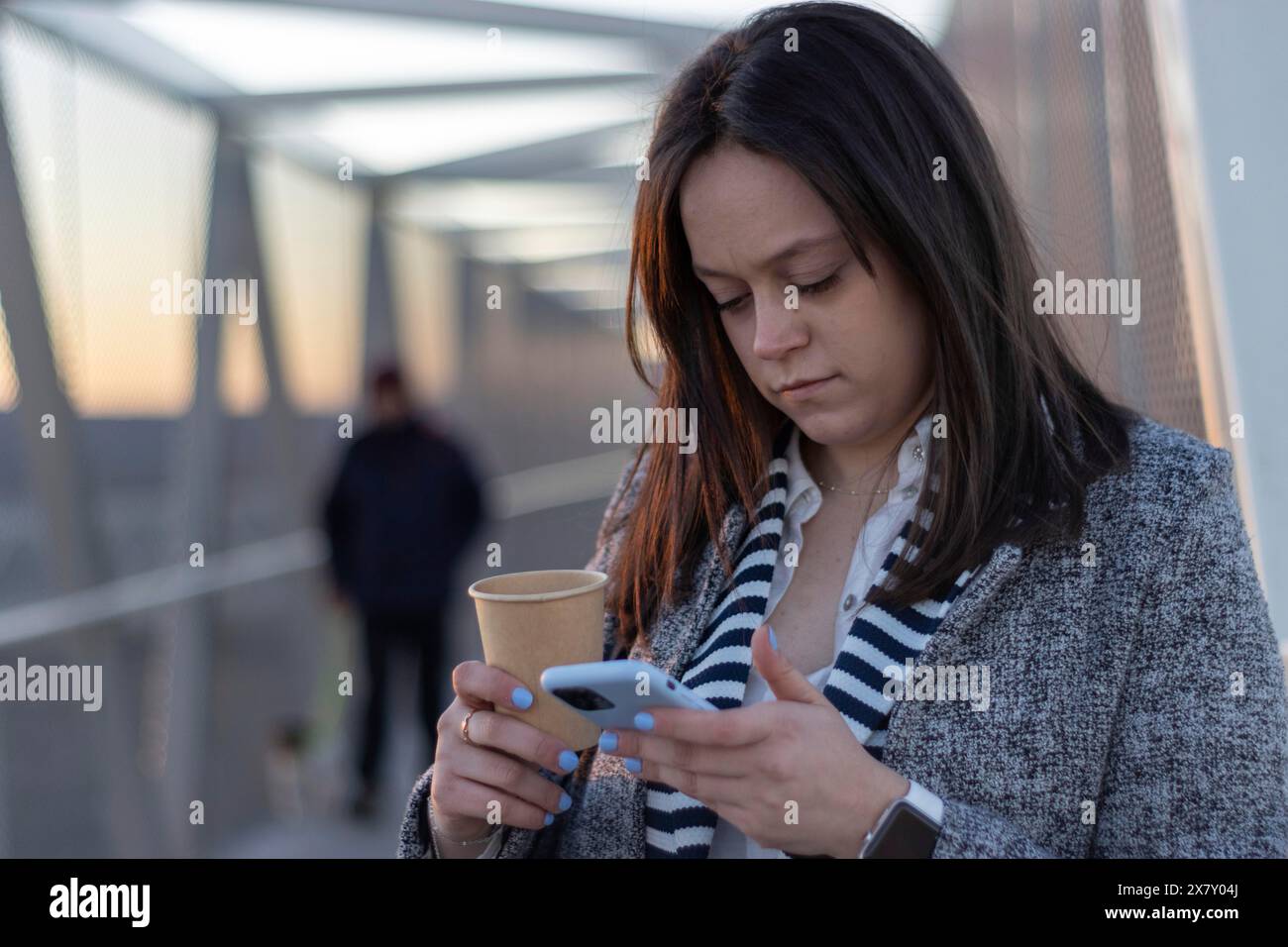 Portrait de jeune femme d'affaires adorable marchant pont dans la journée ensoleillée avec tasse de café à emporter regardant avec le sourire dentelé doux à l'écran de p intelligent Banque D'Images