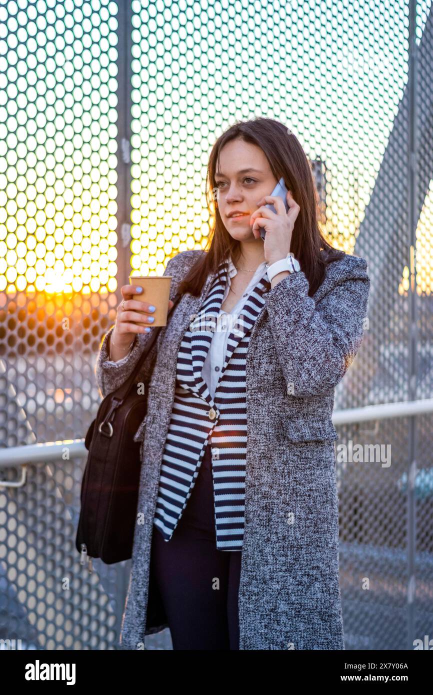Jeune femme parlant au téléphone sur un pont tout en tenant un café. Femme entreprenante sur un pont parlant au téléphone tout en tenant un café Banque D'Images