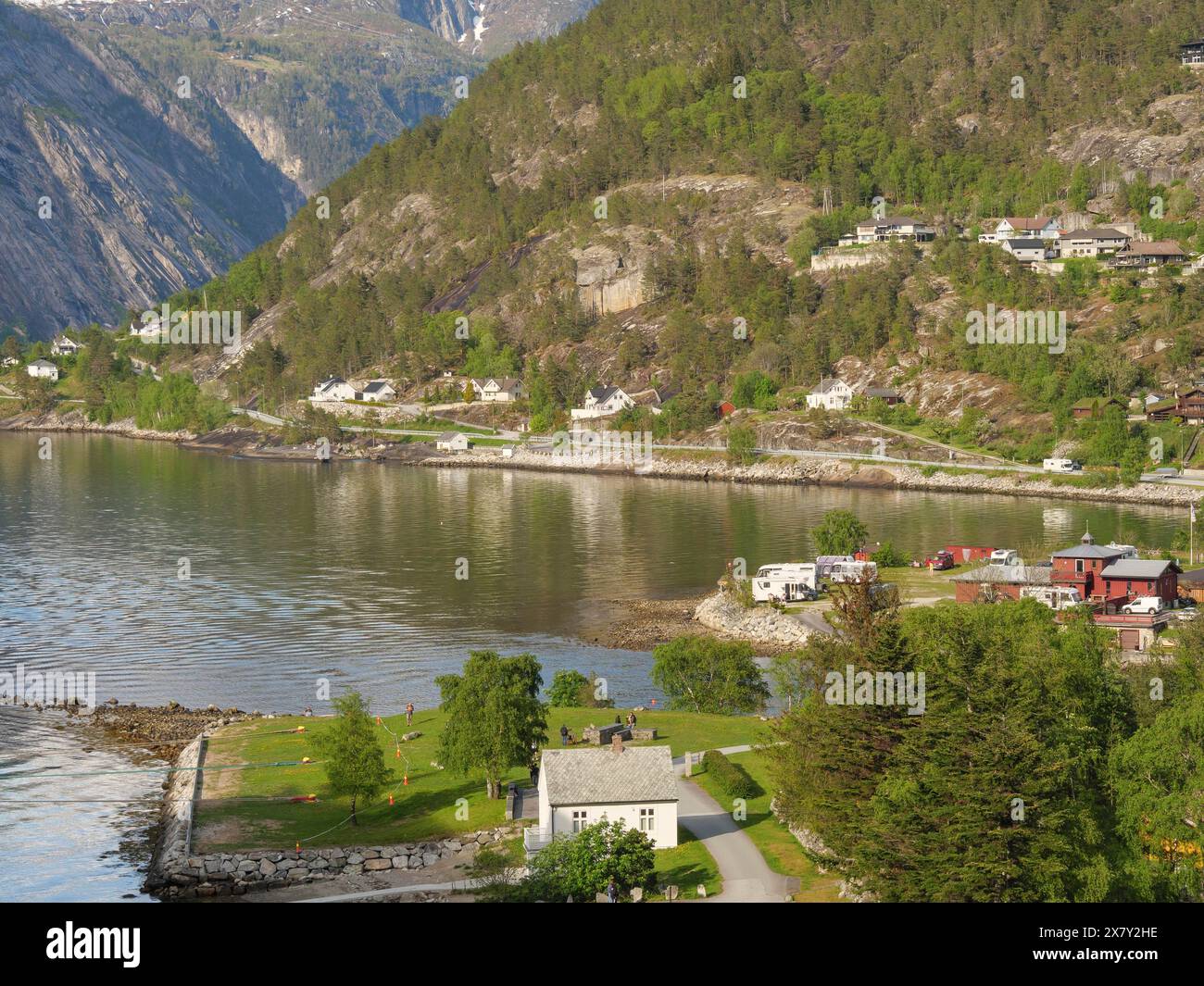 Lac avec des maisons voisines, des arbres verts et un paysage de montagne environnant, petit village dans un fjord en face de hautes montagnes, Eidfjord, norvège Banque D'Images