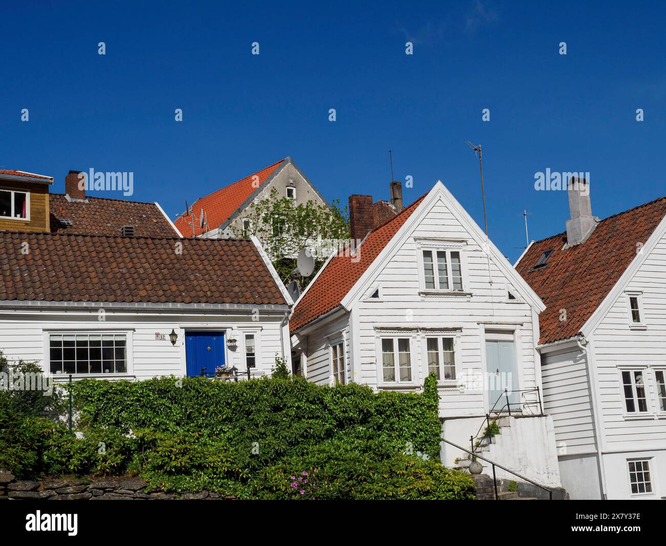 Maisons blanches avec des toits de tuiles et de la végétation contre un ciel bleu, maisons blanches en bois avec des toits rouges contre un ciel bleu, arbres et clôtures blanches le long de t Banque D'Images