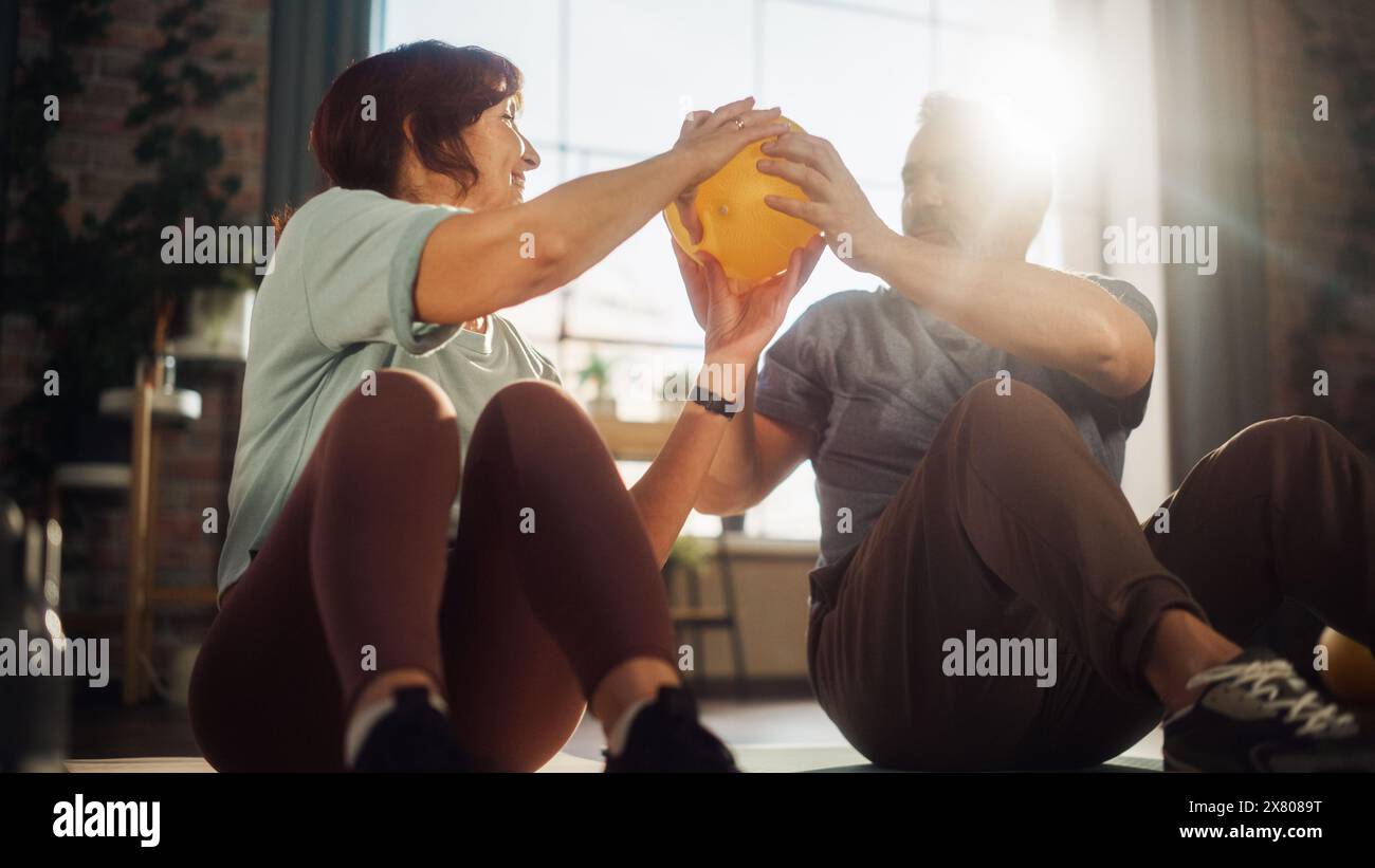Couple senior heureux faisant des exercices de renforcement de noyau ensemble à la maison dans le salon ensoleillé. L'homme et la femme seniors se motivent mutuellement pour être la santé. Concept Lifestyle and Fitness. Banque D'Images