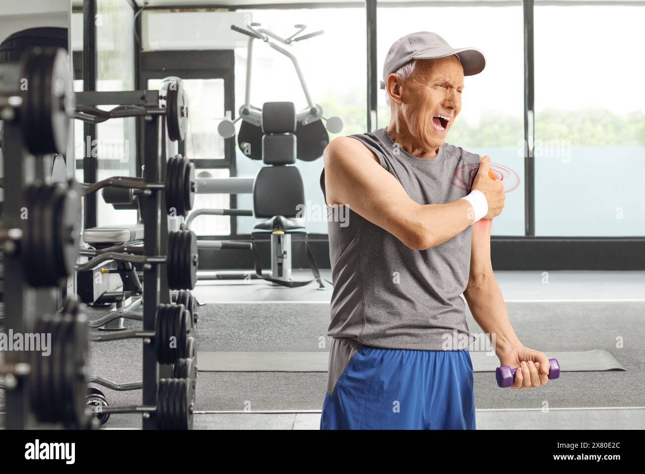 Homme âgé en vêtements de sport s'exerçant dans une salle de gym et tenant son épaule dans la douleur Banque D'Images