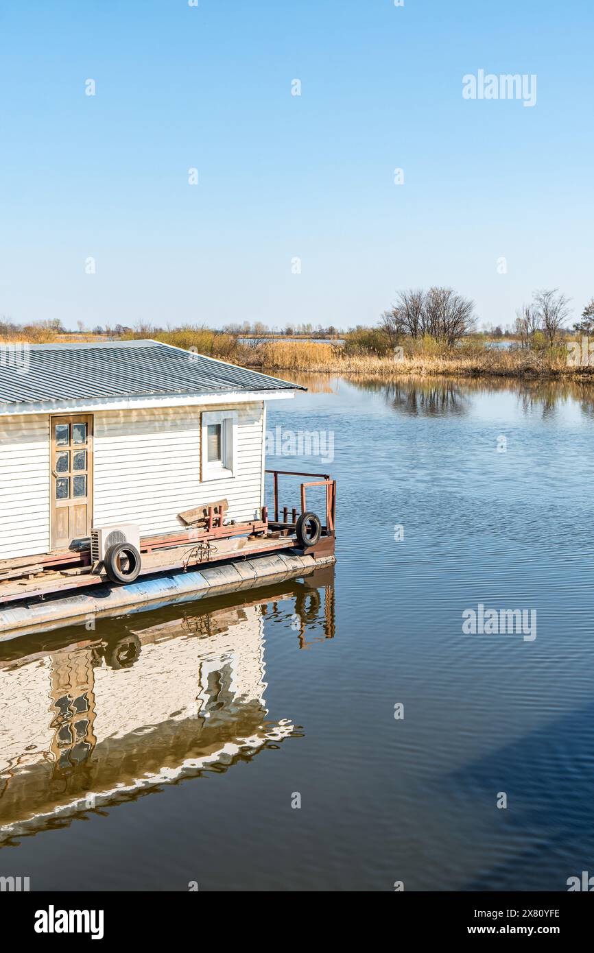 Maison flottante sur l'eau de rivière calme sous ciel clair. Bâtiment pour les pêcheurs et les touristes sur le lac pittoresque. Cabine au bord de la rivière le jour d'automne Banque D'Images