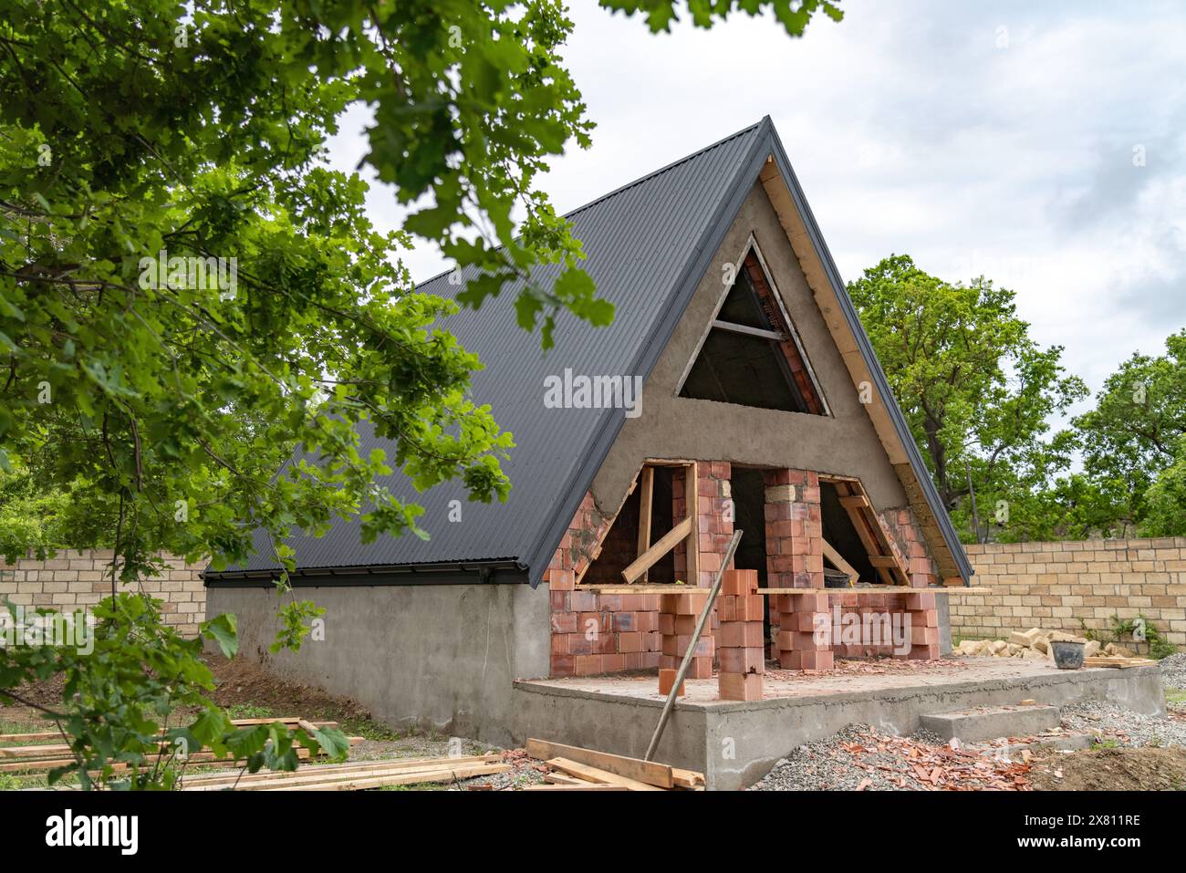 Une petite maison avec un mur de briques et un toit est en construction. Le toit a une forme triangulaire. Banque D'Images