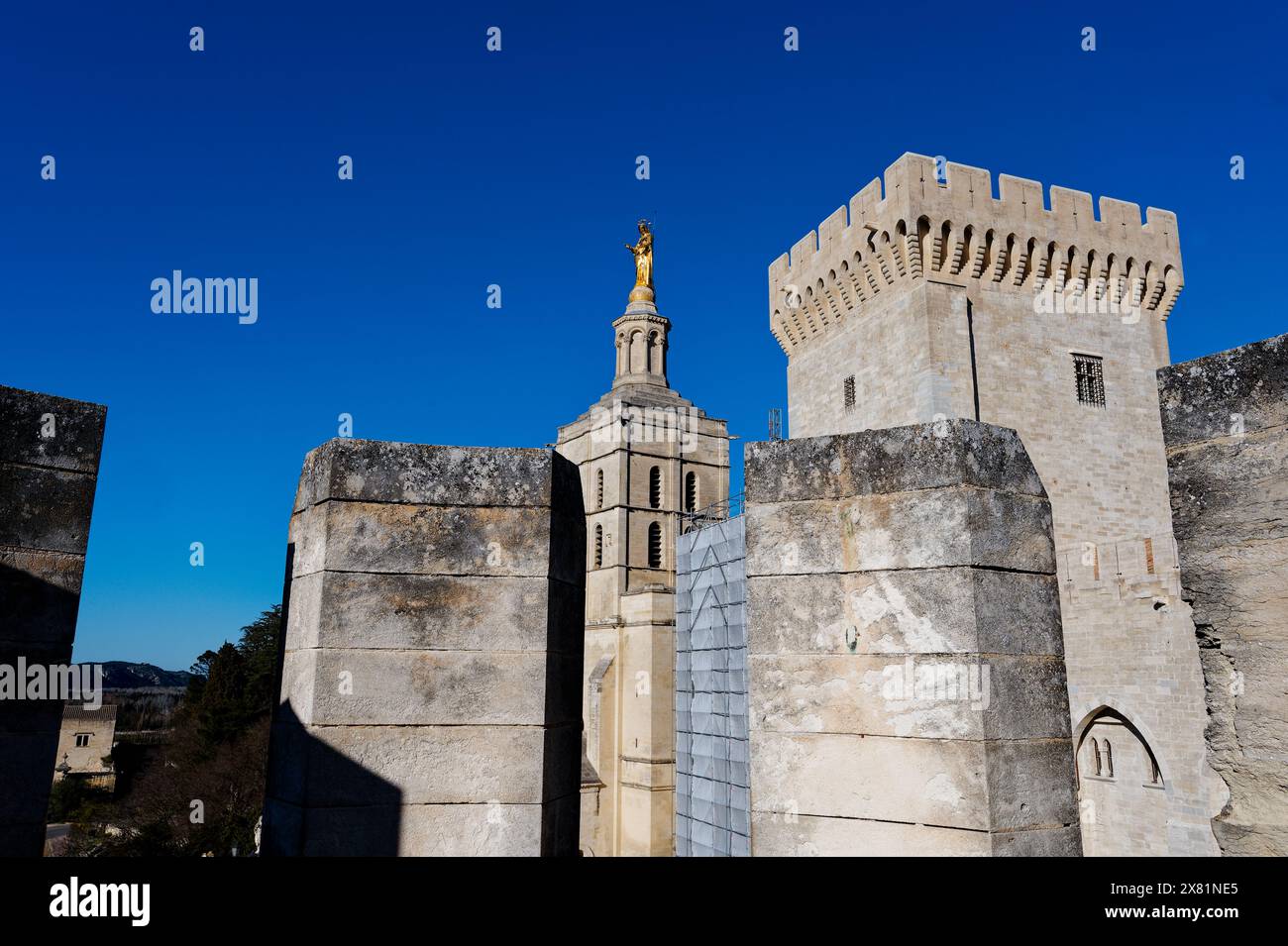 Vue à travers les créneaux d'une tour voisine, la statue dorée de la vierge marie brille brillamment à Avignon sous un vaste ciel bleu profond et clair. Banque D'Images