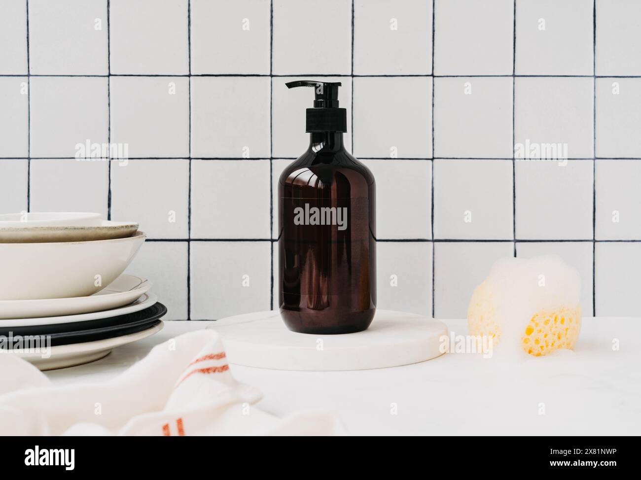 Maquette de bouteille marron pour de détergent à vaisselle naturel dans la cuisine. Bouteille avec détergent à vaisselle sur podium en marbre avec assiettes propres et éponge avec mousse sur wh Banque D'Images