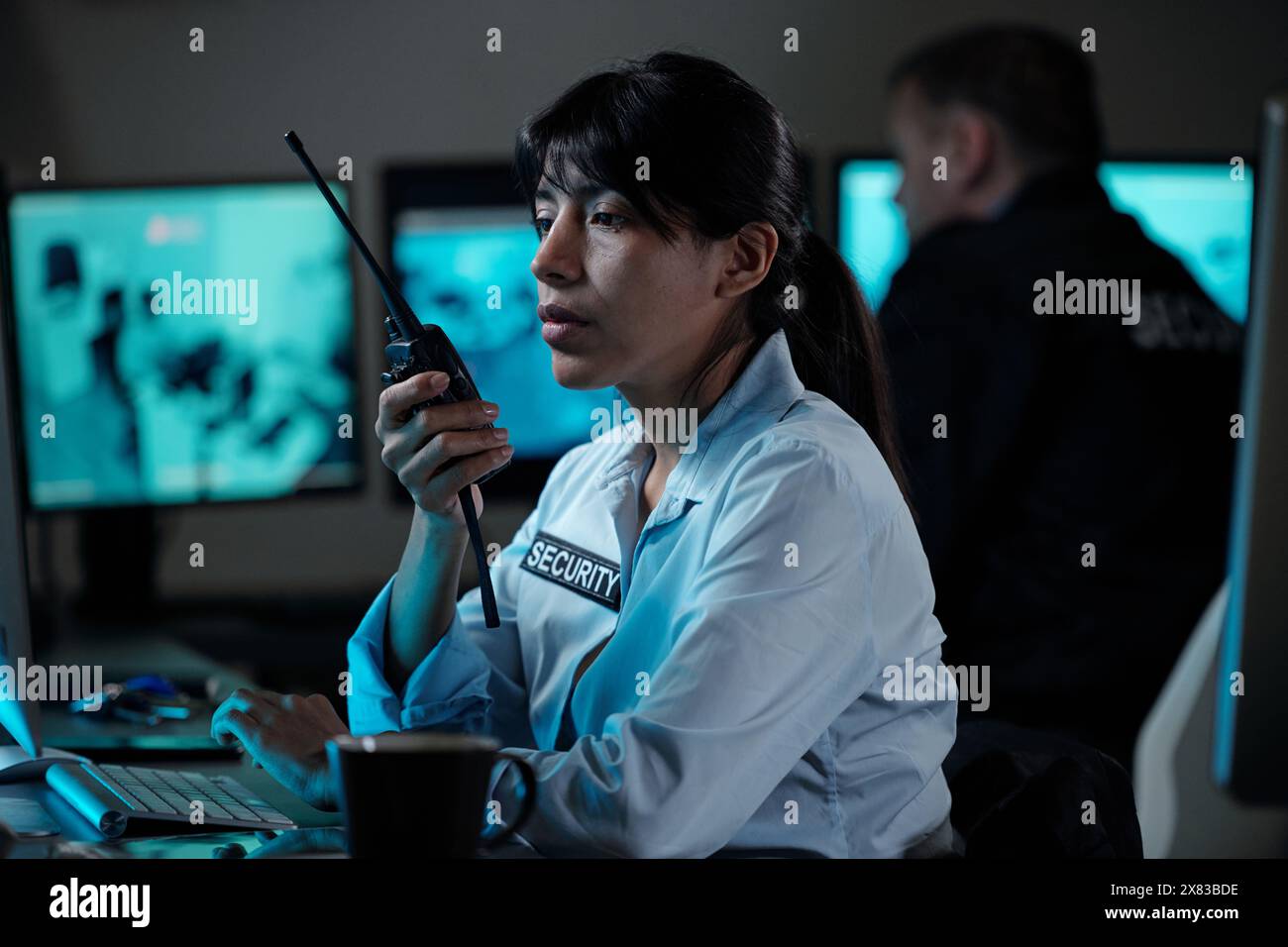 Jeune femme hispanique sérieuse officier de la salle de surveillance signalant la situation sur talkie-walkie tout en regardant l'écran de l'ordinateur Banque D'Images