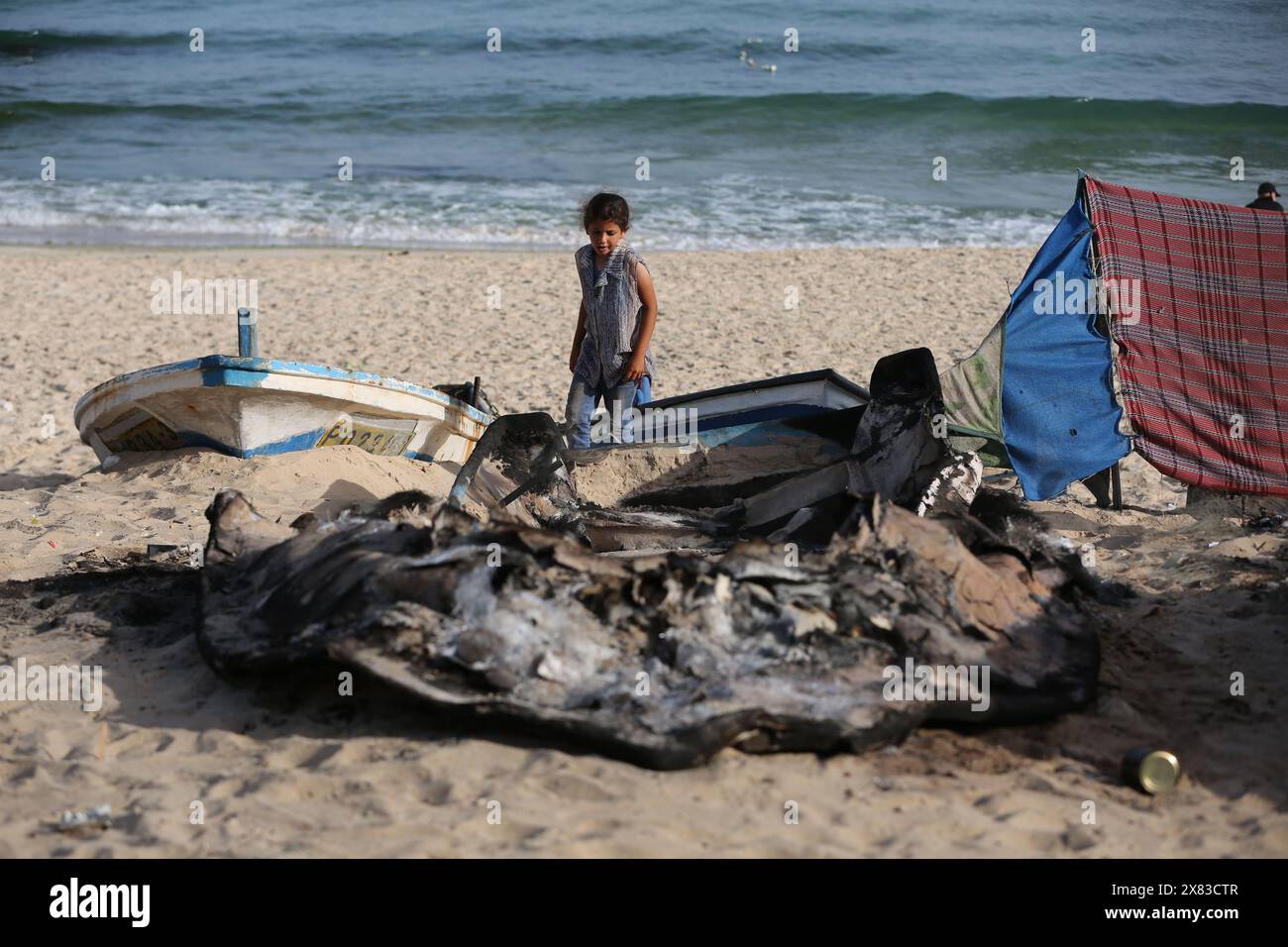 Gaza. 22 mai 2024. Une jeune fille palestinienne regarde un bateau de pêche incendié frappé par des frappes israéliennes sur la côte méditerranéenne de la ville de Rafah, dans le sud de la bande de Gaza, le 22 mai 2024. Au moins 23 Palestiniens ont été tués mercredi dans des raids israéliens sur diverses zones de la bande de Gaza, selon des sources palestiniennes. Crédit : Khaled Omar/Xinhua/Alamy Live News Banque D'Images