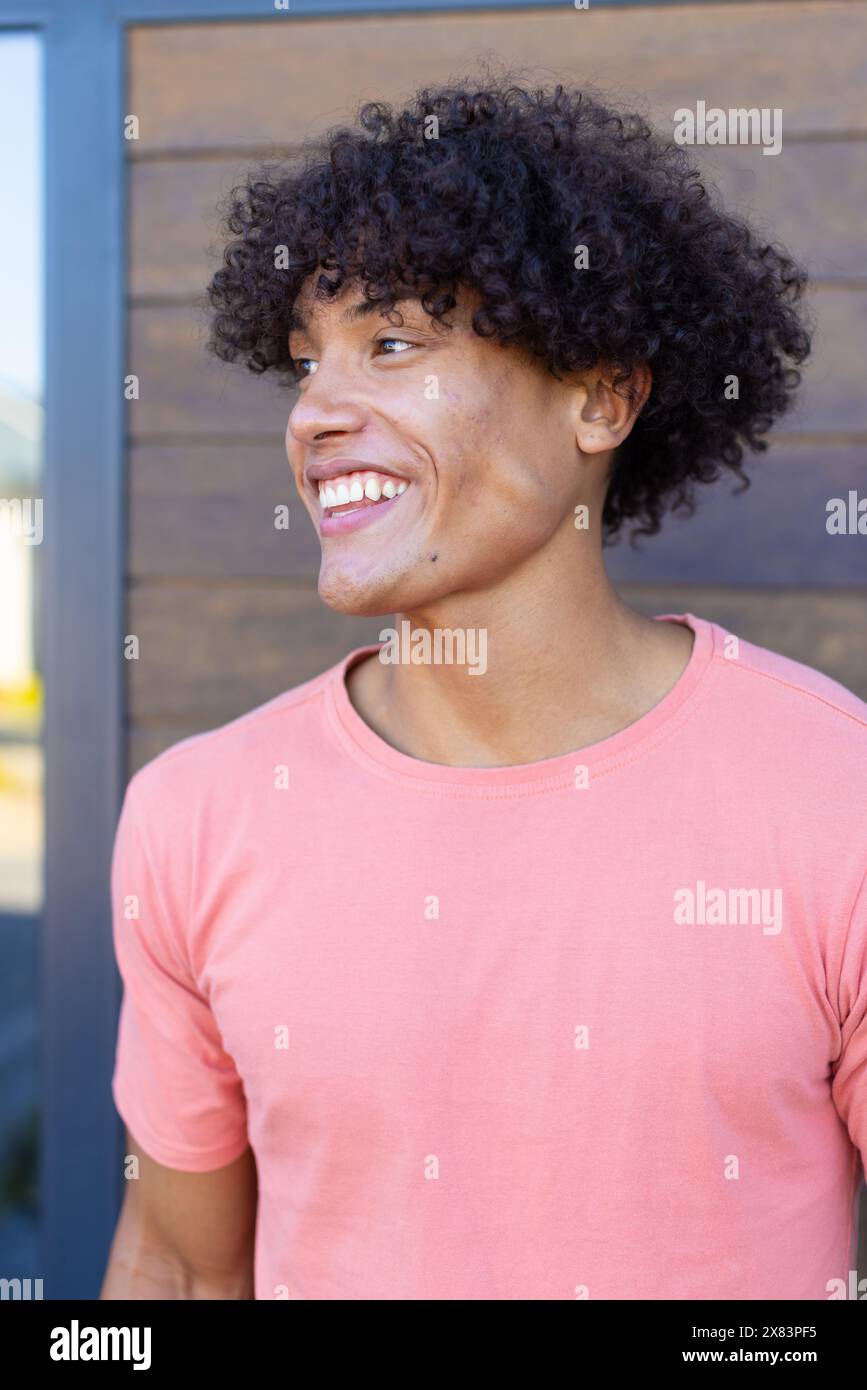 Un jeune homme biracial portant une chemise rose, souriant dehors Banque D'Images