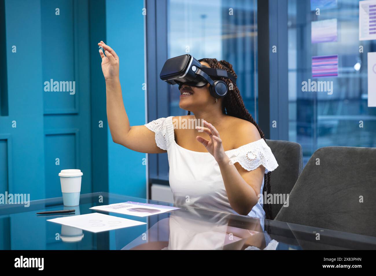 Au bureau moderne pour les affaires, femme biraciale avec des tresses sombres et des yeux bruns utilisant un casque VR Banque D'Images