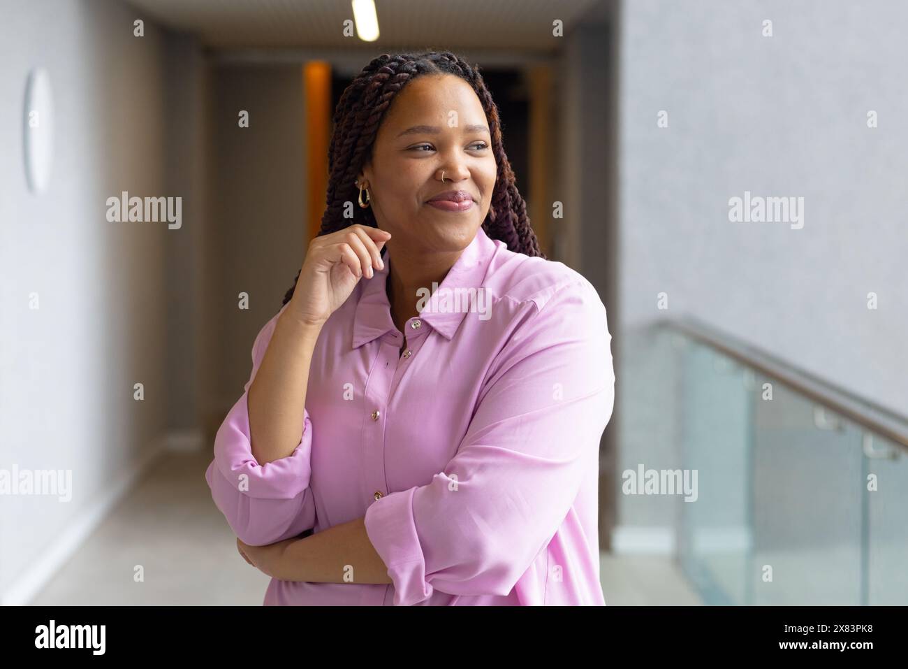 Dans un bureau moderne pour les affaires, une femme biraciale dans une chemise rose clair sourit dans le couloir Banque D'Images