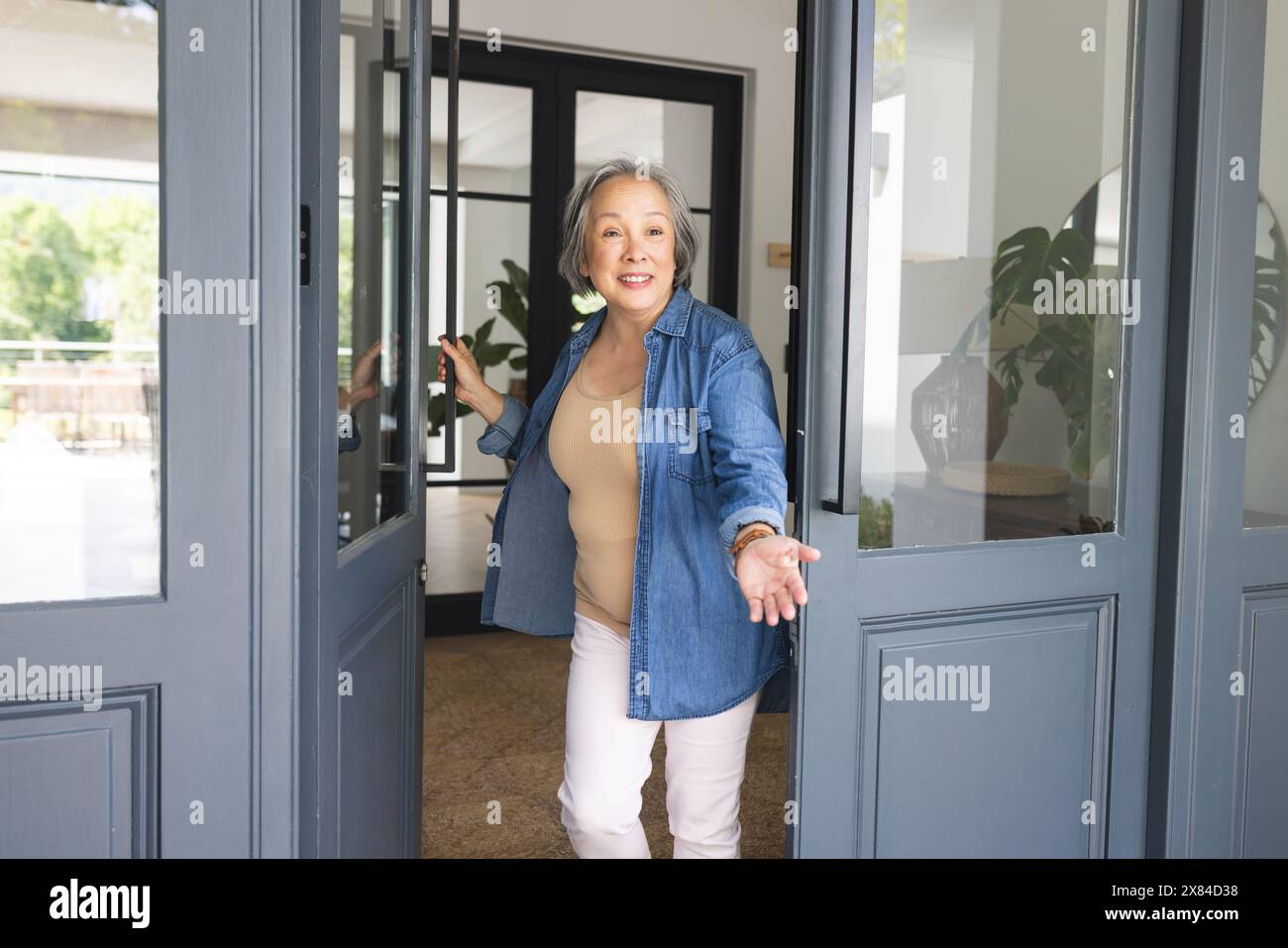 Femme senior asiatique ouvrant la porte d'entrée à la maison, invitant quelqu'un à l'intérieur Banque D'Images