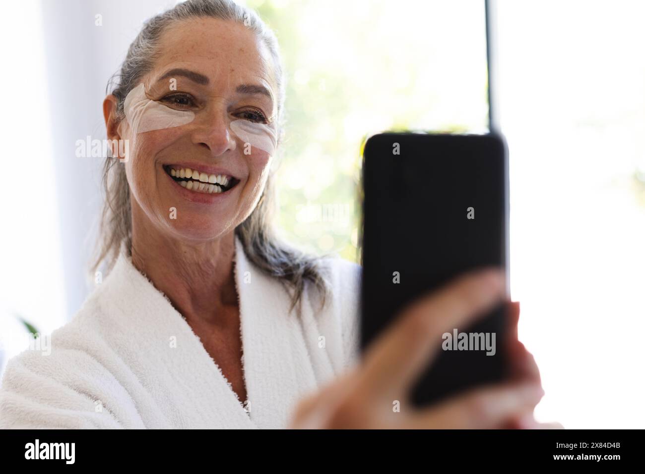 À la salle de bain à la maison, femme caucasienne mature avec crème pour le visage prenant selfie Banque D'Images
