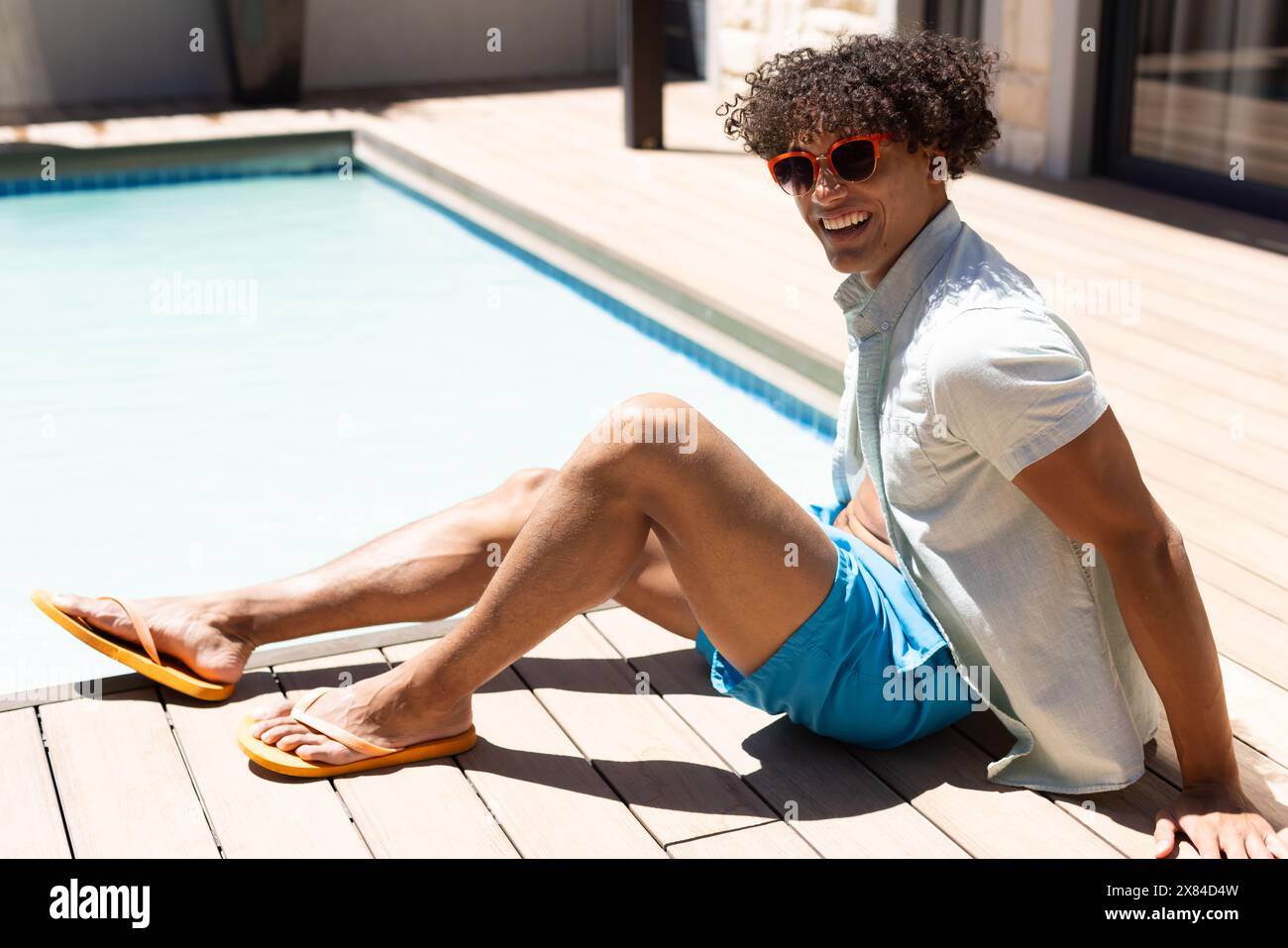 Un jeune homme biracial portant des lunettes de soleil, se relaxant en plein air au bord de la piscine Banque D'Images