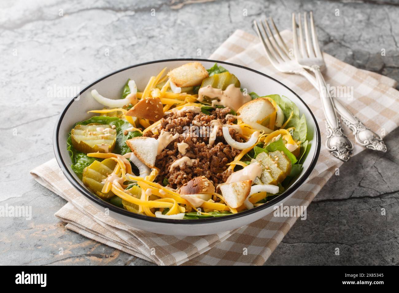 Salade de cheeseburger maison avec laitue, bœuf haché, cornichons, fromage cheddar, oignons et habillé de sauce épicée gros plan sur le bol sur la table. Banque D'Images